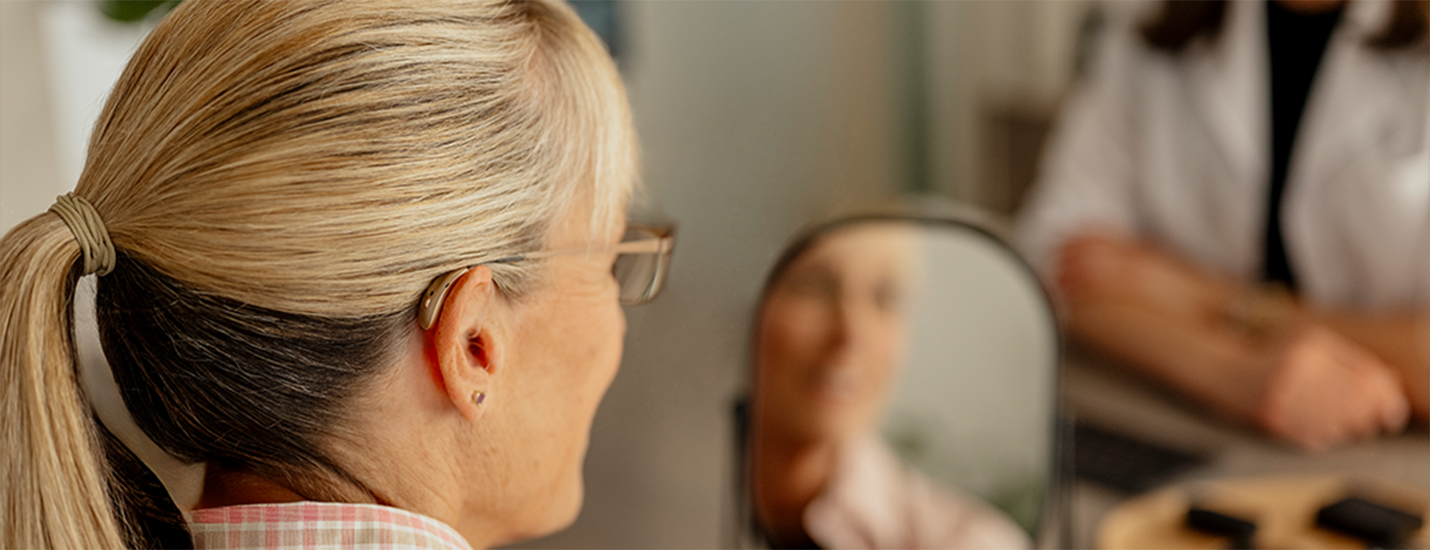 Image of middle aged woman trying on hearing aids in front of her hearing care professional
